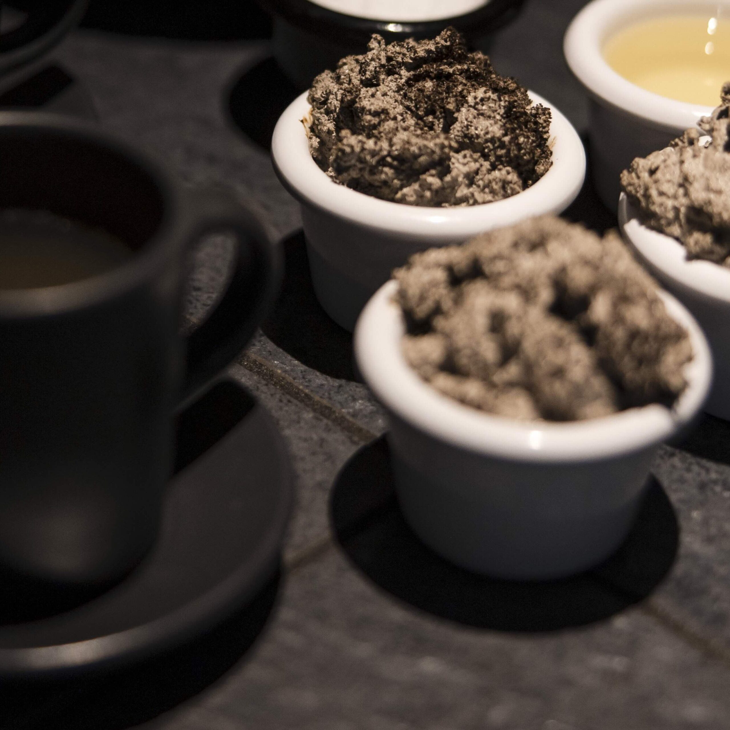 Schwarze Teetassen und Kaffecreme in weißen Schälchen