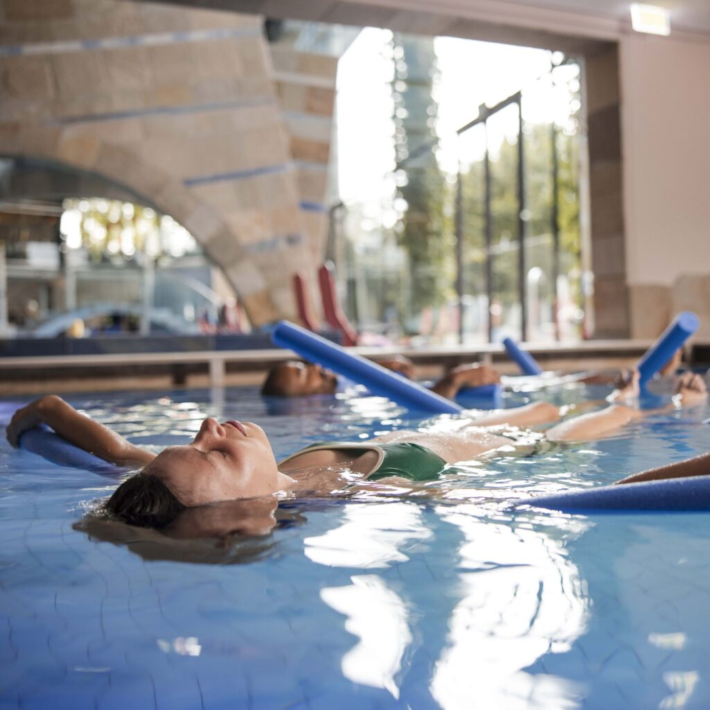 Verschiedene Personen treiben auf Schwimmnudeln in einem Schwimmbecken