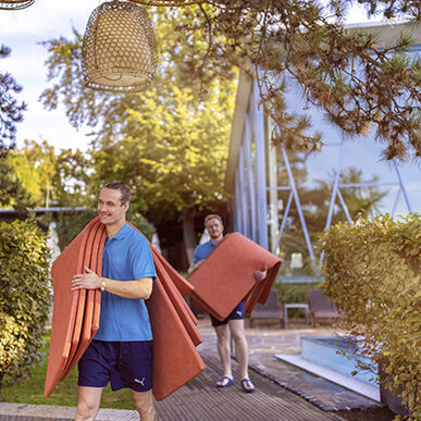 Zwei Mitarbeiter tragen Auflagen für die Sonnenliegen in den Garten der Rosenterrassen